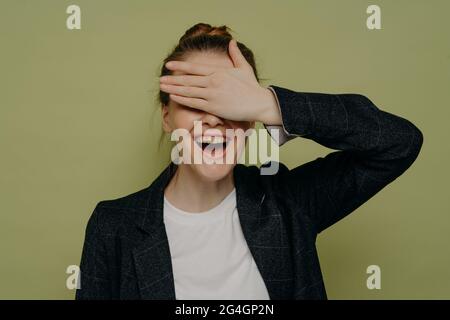 Lachende junge Frau in lässiger Kleidung, die die Augen mit der Hand bedeckt, während sie auf Überraschung wartet Stockfoto