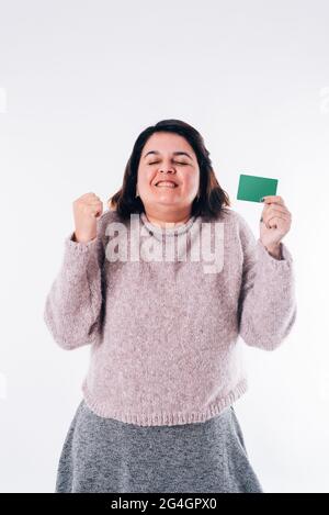 Vertikales Bild einer übertrieben glücklichen Frau, die ihre Augen mit einer Online-Shopping-Karte in der Hand schielt. Einkaufskonzept Stockfoto