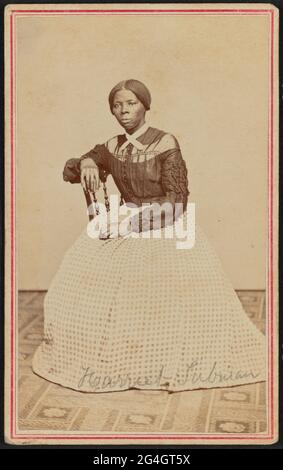 Der afroamerikanische Anti-Sklaverei-Aktivist Harriet Tubman (c1820-1913) wurde in Maryland in die Sklaverei geboren. Sie entkam 1849, wurde eine führende Abolitionistin und war als "Dirigentin" in der Underground Railroad tätig, dem Netzwerk, das entflohenen Sklaven half, in Sicherheit zu kommen. Sie ist leicht nach rechts gedreht positioniert und blickt von der Kamera. Ihre rechte Hand ruht auf dem Rücken eines Holzstuhls und ihre linke Hand ruht auf ihrem Schoß. Ein gemusterter Teppich bedeckt den Boden und die Wand oder fallen hinter ihr ist eine leere helle Farbe. Tubman trägt ein schwarzes Oberteil, das in der Mitte vorne knöpft und hat einen heruntergefallenen Schlitten Stockfoto