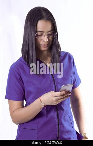 Vertikale Aufnahme einer jungen hispanischen Ärztin/Krankenschwester, die mit ihrem Smartphone eine Brille trägt Stockfoto