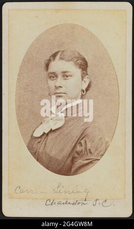Carte-de-Visite von Carrie Lining im Halbportrait. Das Futter ist ein Viertel nach rechts gedreht, wobei ihr Kopf zur Kamera zeigt, obwohl sie etwas aus dem Rahmen sieht. Ihr Haar ist in der Mitte geteilt und am Nacken versammelt. Sie trägt Kreolen und ein dunkles Oberteil mit Stehkragen. Unter dem dunklen Stehkragen ihres Mieder ist ein weißer Kragen, der in einem Bogen am Mittelhals gebunden ist.;handgeschrieben auf dem Foto unter dem Bild ist "Carrie Lining" mit "Charleston, S.C.", das unten auf dem Reittier geschrieben ist. Auf der Rückseite des Fotos befindet sich eine Markierung Stockfoto