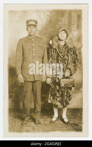 Schwarz-weiße Fotopostkarte, die nie gestempelt und verschickt wurde, aber auf der Rückseite den Namen „Omer Ester“ mit Bleistift geschrieben hat. Das Bild auf der Postkarte zeigt Pullman Porter, Omer Ester, in seiner vollen Portier-Uniform, einschließlich Pullman Porter Cap. Neben ihm steht eine nicht identifizierte afroamerikanische Frau, die einen Samtmantel in voller Länge mit Pelzbesatz am Kragen und an den Ärmeln trägt. Sie trägt einen Frauenhut im Stil der 1920er Jahre und hält eine Handtasche in ihrer rechten Hand. Sie befinden sich in einem Fotostudio, das vor einer gemalten Kulisse mit einem Karpfen im orientalischen Stil steht Stockfoto