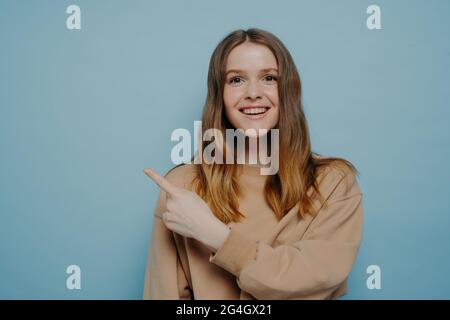 Positive junge Frau zeigt den Finger nach oben und zieht Aufmerksamkeit auf sich Stockfoto