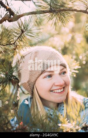 Junge Kaukasische Dame In Weißer Jacke Und Braunem Hut, Die In Der Nähe Von Pine Tree Posiert. Nahaufnahme Porträt. Schöne junge Frau lächelnd Stockfoto