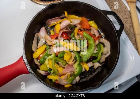 Draufsicht auf Garnelen und Paprika, die in einer gusseisernen Pfanne auf einem weißen Herd kochen Stockfoto