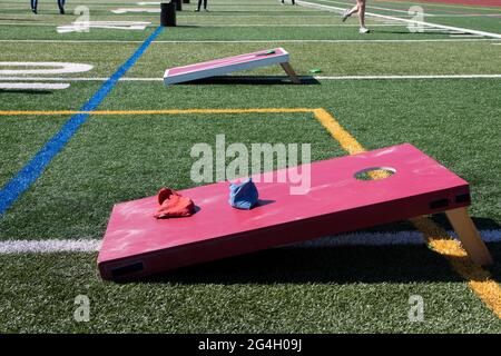 Ein Schulrasenfeld ist mit rot-weißen Holzkornhole-Spielen und anderen Hinterhof-Spielen für Kinder eingerichtet, um zu spielen und Spaß in der Sonne zu haben. Stockfoto