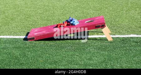 Seitenansicht eines hausgemachten soliden roten Cornhole-Spiels auf einem grünen Rasenfeld mit blauen und roten Bohnenbeuteln, die oben ruhen. Stockfoto