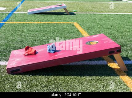 Seitenansicht von zwei selbstgemachten Cornhole-Spielen aus rotem Holz auf einem grünen Rasenfeld mit blauen und roten Bohnenbeuteln. Stockfoto