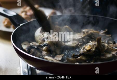 Draufsicht auf frisch geschnittenen Pilzen werden in Bratpfanne mit Dampf aus und Holzlöffel gekocht wird für das Mischen von Gemüse zeigt Hausmannskost V verwendet Stockfoto