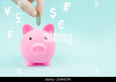Hand, die eine Münze in Sparschwein mit digitalen Hologramm-Weltwährungen auf blauem Hintergrund. Finanzielle Ersparnisse und die Bankenwirtschaft Stockfoto