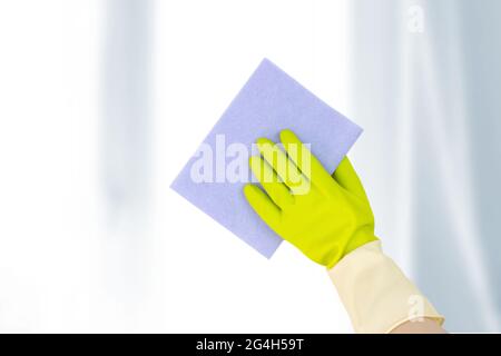 Fenster mit Waschmotiven. Draufsicht der Hand in gelben Gummihandschuhen, die einen Lappen halten und die Fensterfläche abwischen. Frühjahrsputz-Konzept. Stockfoto