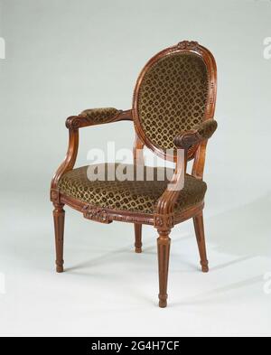 . Sessel aus Mahagoni. Die Möbel sind bedeckt und ruhen auf konischen Beinen mit Kaneluren. Das Sitzfenster ist vorne abgerundet. Der Vordersitz ist in der Mitte mit einer Schleife verziert. Die quadratischen abgebrochenen Armlehnen-Tricks tragen c-förmige Armlehnen mit Kissen, die in einer Spirale enden. Das ovale, geheilte Rückfenster ist mit Perlenkette verziert und in der Mitte oben mit einer Schleife. Stockfoto