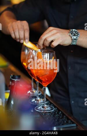 Drei Gläser Cocktails an der Bar. Barkeeper gießt ein Glas Sekt mit Aperol. Stockfoto