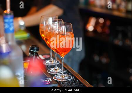 Drei Gläser Cocktails an der Bar. Barkeeper gießt ein Glas Sekt mit Aperol. Stockfoto