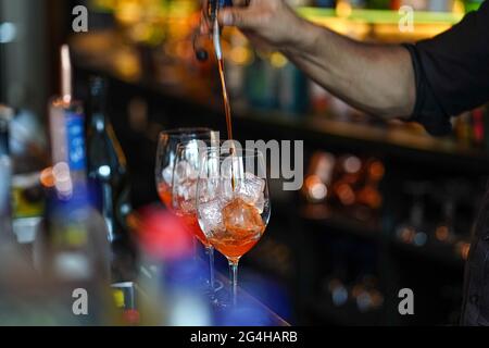 Drei Gläser Cocktails an der Bar. Barkeeper gießt ein Glas Sekt mit Aperol. Stockfoto