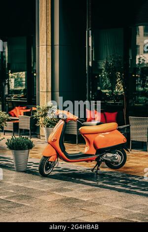 Orange Scooter parkte an regnerischen Tagen in der Nähe des Cafés. Vintage-Karte Stockfoto