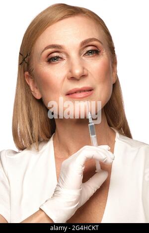 Porträt einer schönen älteren Frau in einem weißen Hemd mit klassischem Make-up und blondem Haar mit Spritze in den Händen Stockfoto