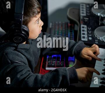 Portrait eines kleinen Jungen, der mit Kopfhörern Musik hört und Keyboards im Aufnahmestudio spielt Stockfoto