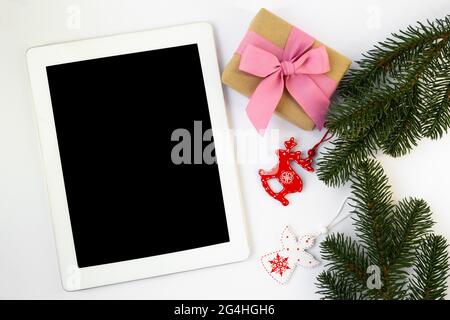 Tablet, Geschenkverpackung, Tannenzweige mit Weihnachtsspielzeug. Online-Shopping. Online-Auswahl von Geschenken Stockfoto