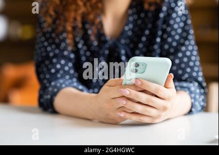 Weibliche Hände halten trendige Smartphone. Frau im dunklen Dotter-Hemd benutzt Telefon, tippt E-Mail, Nachrichten und chattet online, scrollt in den Neuigkeiten, ein Gesicht ist nicht sichtbar, Nahaufnahme Stockfoto