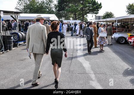 Menschen in Vintage-Kleidung wandern während des Goodwood Revival 2011 im Fahrerlager-Bereich. Männer und Frauen in klassischem Kleid mit Rennwagen Stockfoto