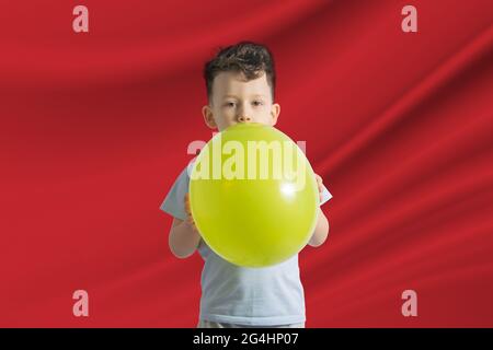 Kindertag in Marokko. Weißer Junge mit einem Ballon auf dem Hintergrund der Flagge Marokkos. Kindertagesfeier Konzept. Stockfoto