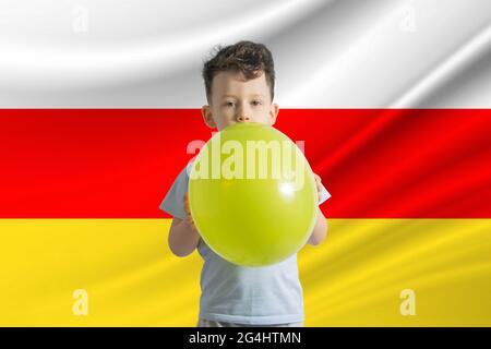 Kindertag in Südossetien. Weißer Junge mit einem Ballon auf dem Hintergrund der Flagge von Südossetien. Kindertagesfeier Konzept. Stockfoto