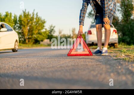 Junger Mann hält ein rotes Dreieck und legt es auf die Straße, das Zeichen eines Autounfalls Stockfoto