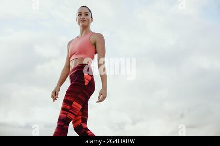 Sportliche Frau in Fitnesskleidung, die draußen steht. Fitness-Frau, die wegschaut, während sie gegen den Himmel trainiert. Stockfoto