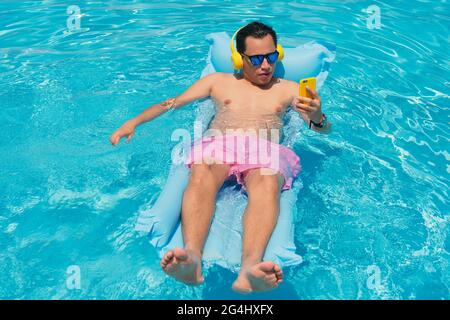 Hispanic Mann sonnenbaden am Pool und halten Handy in der Hand Stockfoto
