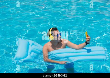 Mann, der sich am Pool sonnt und das Handy in der Hand hält Stockfoto