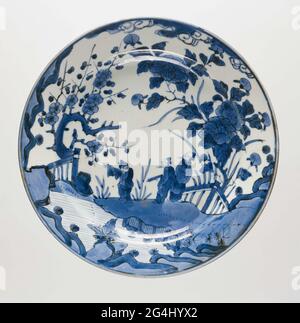 . Schale aus Porzellan, in Unterglasur blau gemalt. Auf der Vorderseite eine kontinuierliche Darstellung von drei Personen in einer Landschaft am Ufer eines Flusses. Ein Mann hat eine Rolle in der Hand, ein anderer ist nahe am Wasser und zeigt auf die gegenüberliegende Seite. Rechts von der Gruppe eine große Pfingstrose hinter einem Zaun; links ein prunusbaum hinter einem Zaun. Fünf Preen auf der Unterseite. Altes Etikett auf der Unterseite mit „P [?] 8031 / Imari / + - 1700 / F 475'. Arita, blau-weiß. Stockfoto