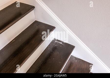 Weiß gestrichene und dunkel gebeizte Holztreppe in einem Neubau-Haus mit Blechstaub aus dem Loch in der Wand darüber Stockfoto