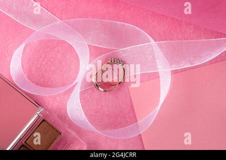 Goldene Ringe liegen auf einer rosa Tischoberfläche. Stockfoto