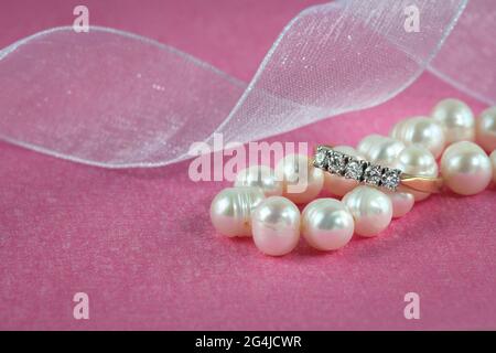 Ein schöner Goldring mit Edelsteinen und einer Perlenkette. Schmuck auf rosa Hintergrund. Stockfoto