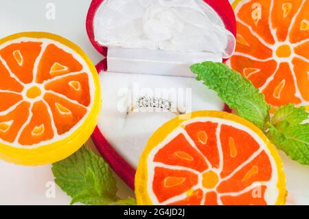 Ein Diamantring in einer roten Schachtel, umgeben von einer ungewöhnlichen Umgebung aus süßen Bonbons und frischen Minzblättern. Süße Liebe. Stockfoto