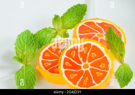 Ein Diamantring, umgeben von einer ungewöhnlichen Umgebung aus süßen Bonbons und frischen Minzblättern. Süße Liebe. Stockfoto