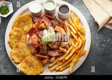 Draufsicht auf einen Teller mit gegrilltem Fleisch, Saucen und pommes frites Stockfoto