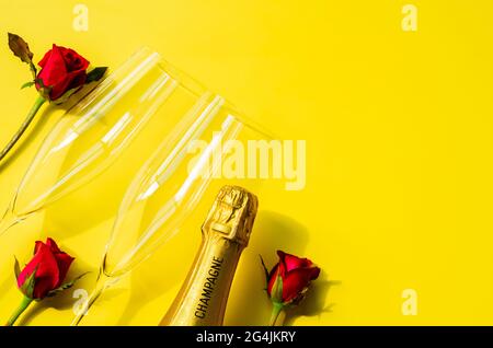 Champagnerflasche mit zwei Gläsern und Rosenblüten auf gelbem Hintergrund Stockfoto