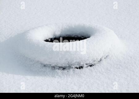 Gummireifen liegt unter dem frisch gefallenen weißen Schnee. Schneefall, heftige Schneefälle, als texturierter Hintergrund. Stockfoto