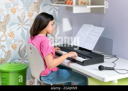 Ein junges Mädchen, das auf einer elektronischen Tastatur Musik spielt und Noten über dem Instrument folgt, in einem Konzept eines Freizeithobby oder Learni Stockfoto