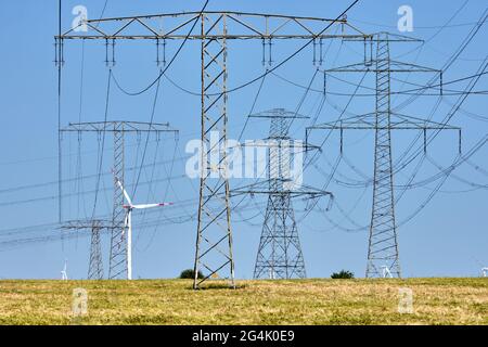Strommasten und Stromleitungen mit Windturbinen im Hintergrund, in Deutschland gesehen Stockfoto