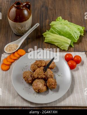 Draufsicht auf einen Teller mit Fleischbällchen mit Kirschtomaten, in Scheiben geschnittenen Karotten und Salat auf einem Holztisch Stockfoto