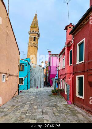 Farbenfrohe Häuser in einer kleinen traditionellen Straße mit der Spitze einer Kirche auf der Insel Burano, Venedig, Italien Stockfoto