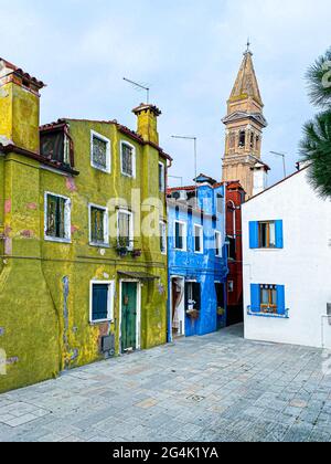 Farbenfrohe Häuser in einer kleinen traditionellen Straße mit der Spitze einer Kirche auf der Insel Burano, Venedig, Italien Stockfoto