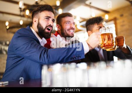 Männerfans schreien und beobachten Fußball im Fernsehen und trinken Bier in einer Kneipe Stockfoto