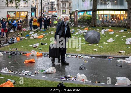 Ein Mann, der seinen Reisekoffer trägt, durchläuft all die zerbrochenen Flaschen und den Müll, die schottische Fußballfans auf dem Leicester Square hinterlassen haben Stockfoto