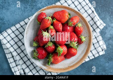 Frische Erdbeeren in Keramikschale auf blauem Hintergrund, Draufsicht. Gesunde saftige Sommerbeeren Stockfoto