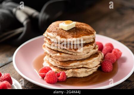 Gesunde Haferpfannkuchen mit Himbeeren und Ahornsirup auf einem rosa Teller, Holztisch Hintergrund Stockfoto