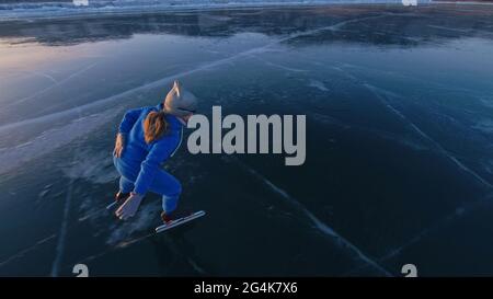 Das Kind trainiert auf Eisschnelllauf. Das Mädchen Schlittschuhe im Winter in Sportbekleidung, Sportbrille, Anzug. Zeitlupe im Freien. Stockfoto